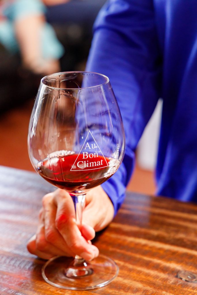 A hand holding a wine glass with red wine inside and Au Bon Climat on the glass.