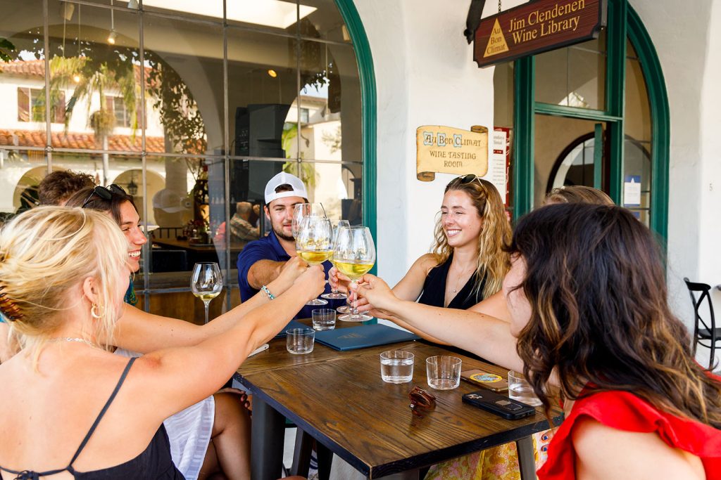 Wine Tasters clinking glasses of white wine at an outdoor table at our Santa Barbara Wine Tasting Room for Au Bon Climat and Clendenen Family Vineyards
