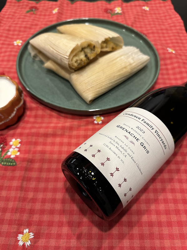 Bottle of Clendenen Family Vineyards 2023 Grenache Gris paired with homemade tamales on a green ceramic plate over a festive red tablecloth.