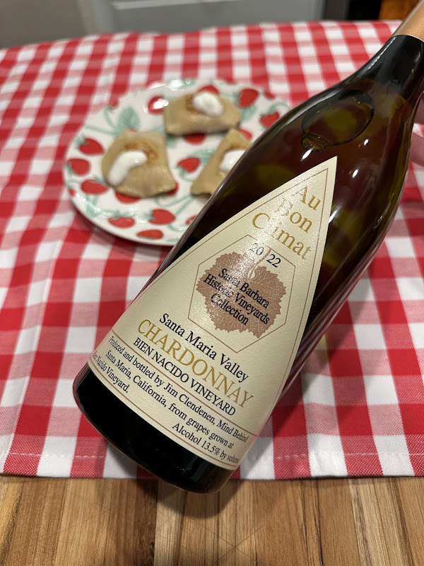 Au Bon Climat 2022 Bien Nacido Vineyard Chardonnay paired with holiday tamales topped with sour cream on a festive red-and-white gingham tablecloth.